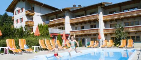 A swimming pool area with lounge chairs and a building with balconies in the background.