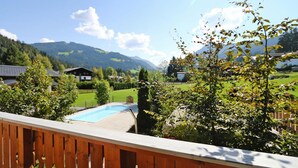 Una piscina con bordo in legno, immersa nel verde e circondata da case in zona montana.