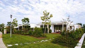 Ein modernes Gebäude mit gepflegtem Rasen, einem Kiesweg und einer kleinen Gartenanlage mit verschiedenen Pflanzen.