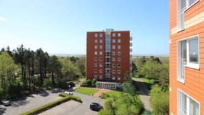 A multi-story building with a central entrance, surrounded by greenery and a parking area. - Ferienwohnung in St. Peter-ording (St. Peter-Ording)