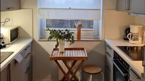 Une cuisine compacte avec une fenêtre, un four à micro-ondes, une machine à café et une petite table agrémentée d’une plante.