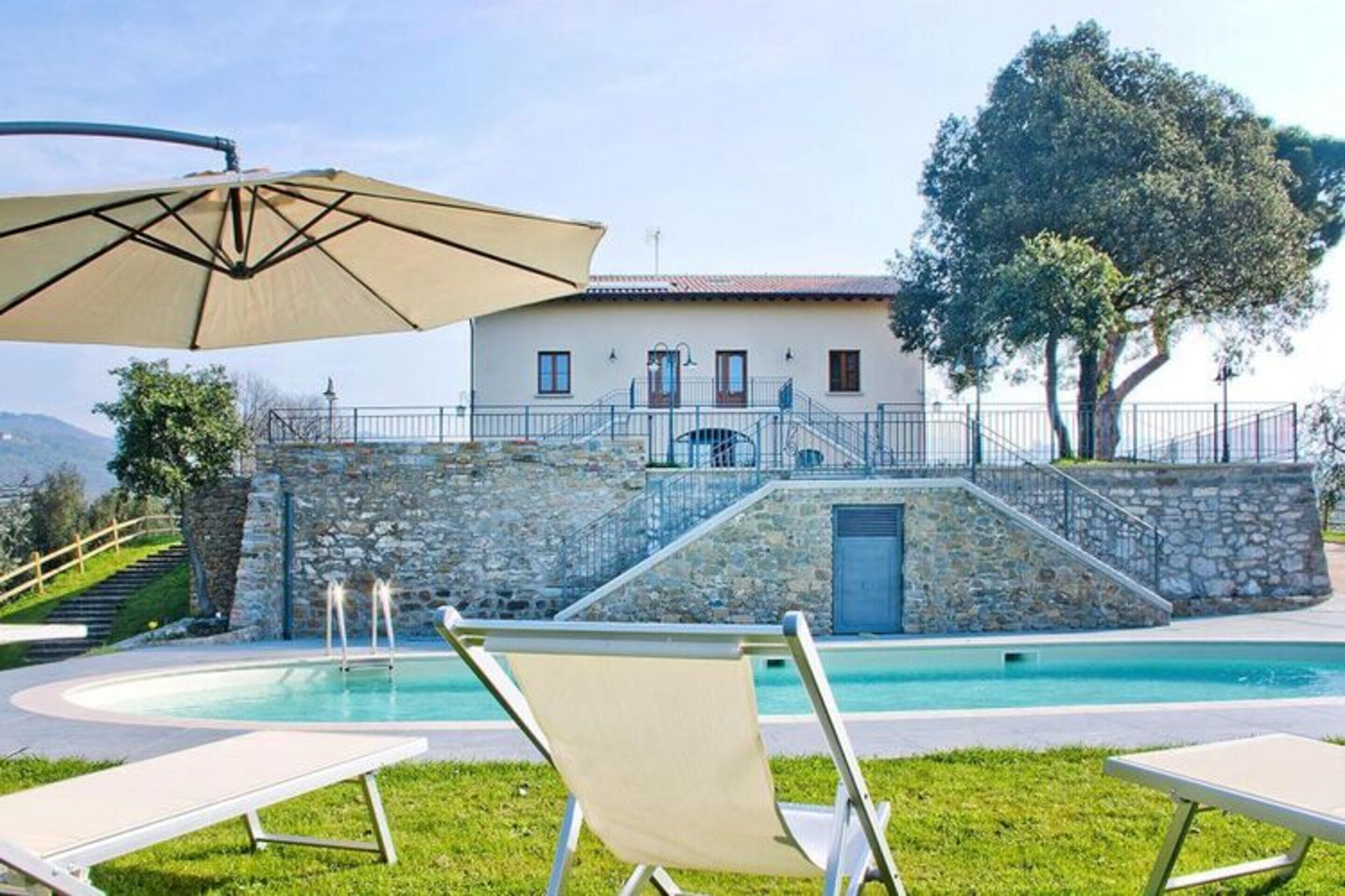 A pool area with lounge chairs, a stone wall, and a building with a staircase leading to a door.