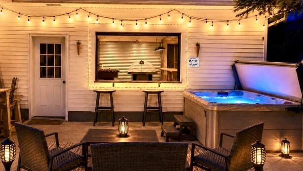 An outdoor patio with a hot tub, string lights, and wicker furniture. - Gondola House | Hot tub, Arcade, Walkable Getaway, Fun Central! Game Room, Hot Tub, Steps to Village... (Ellicottville)