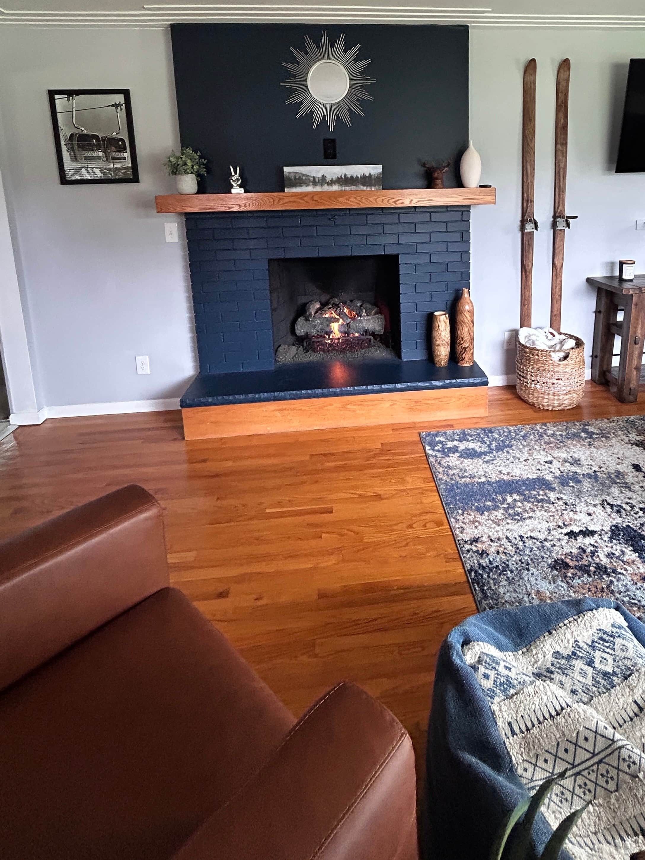 A living room with a fireplace, wooden flooring, a blue accent wall, and a patterned rug.