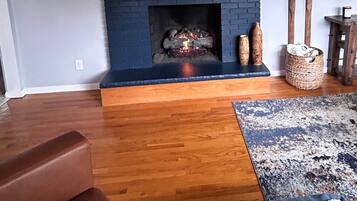 A living room with a fireplace, wooden flooring, a blue accent wall, and a patterned rug.