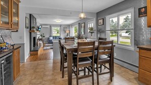 A modern kitchen with a dining area, wooden cabinets, and a view of the outdoors. - Gondola House | Hot tub, Arcade, Walkable Getaway, Fun Central! Game Room, Hot Tub, Steps to Village... (Ellicottville)