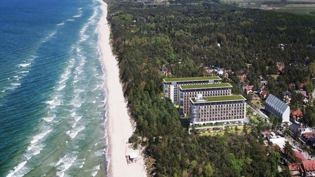 An aerial view of a coastal hotel with a long beachfront, dense forested area, and modern buildings with green roofs. - Apartment Close to the Sea, With Pool and Sauna (Rewal)