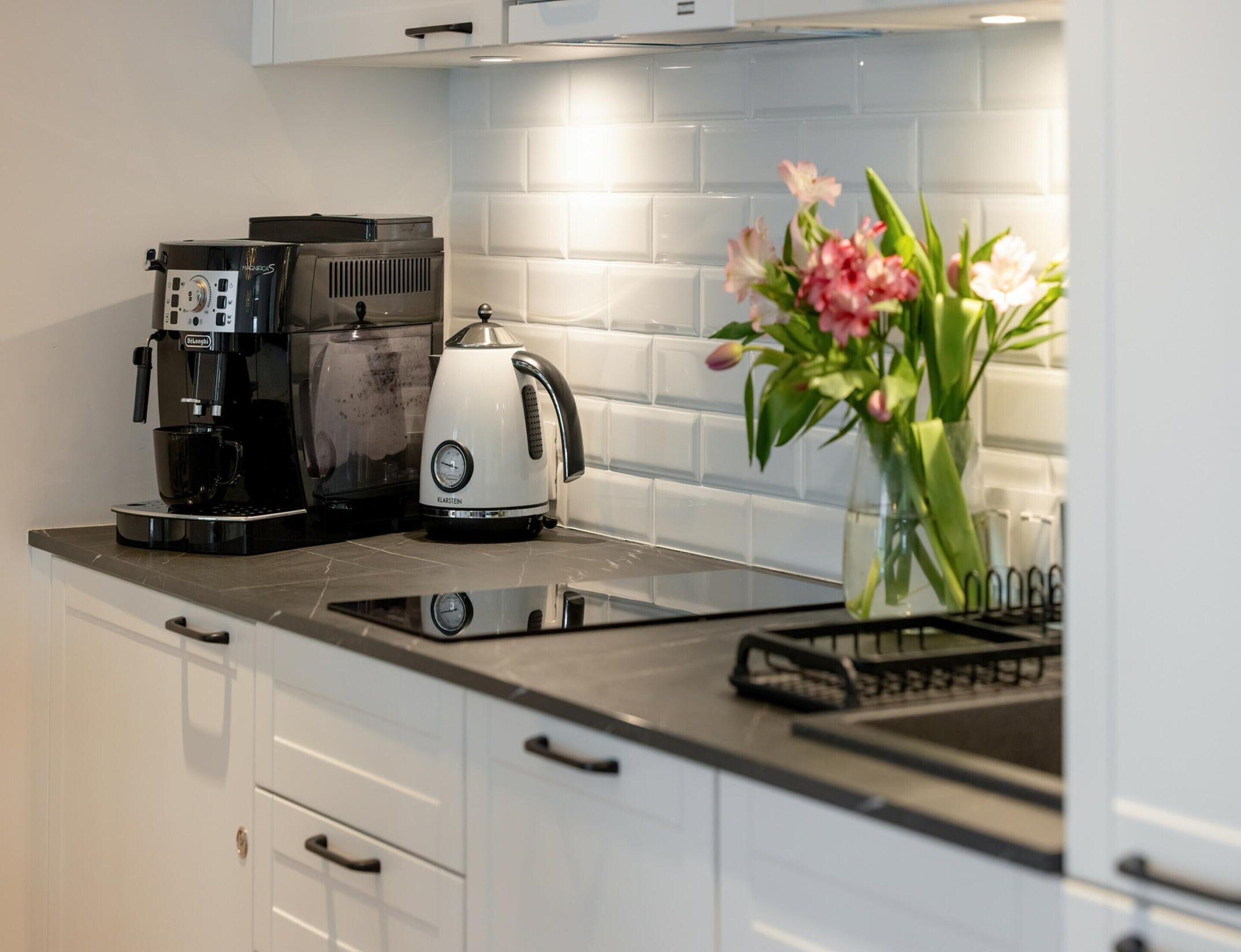 A modern kitchen with a coffee maker, kettle, and a vase with flowers on the counter.