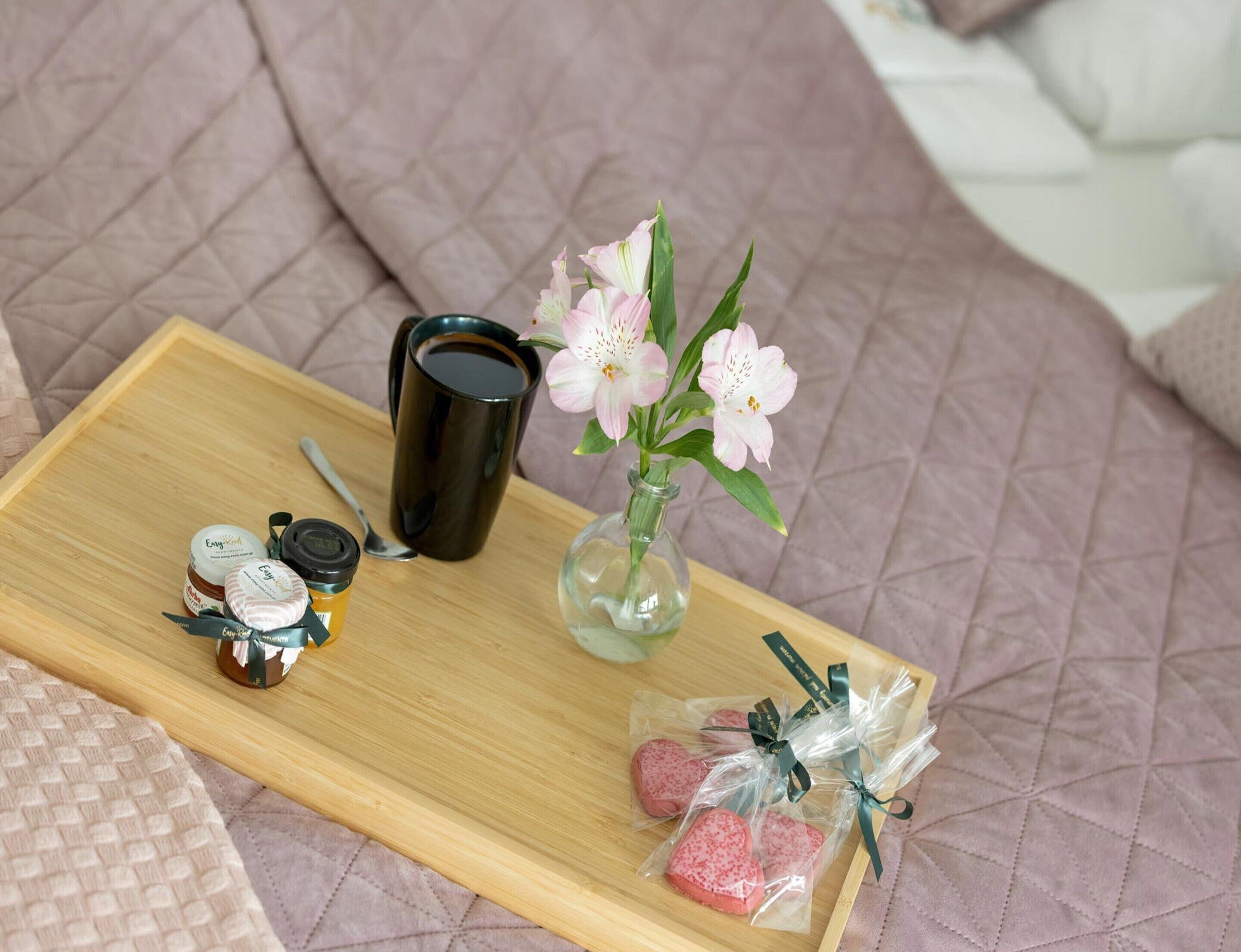 Un vassoio con una tazza di caffè, un barattolo di marmellata, un piccolo vaso con fiori e cioccolatini a forma di cuore.