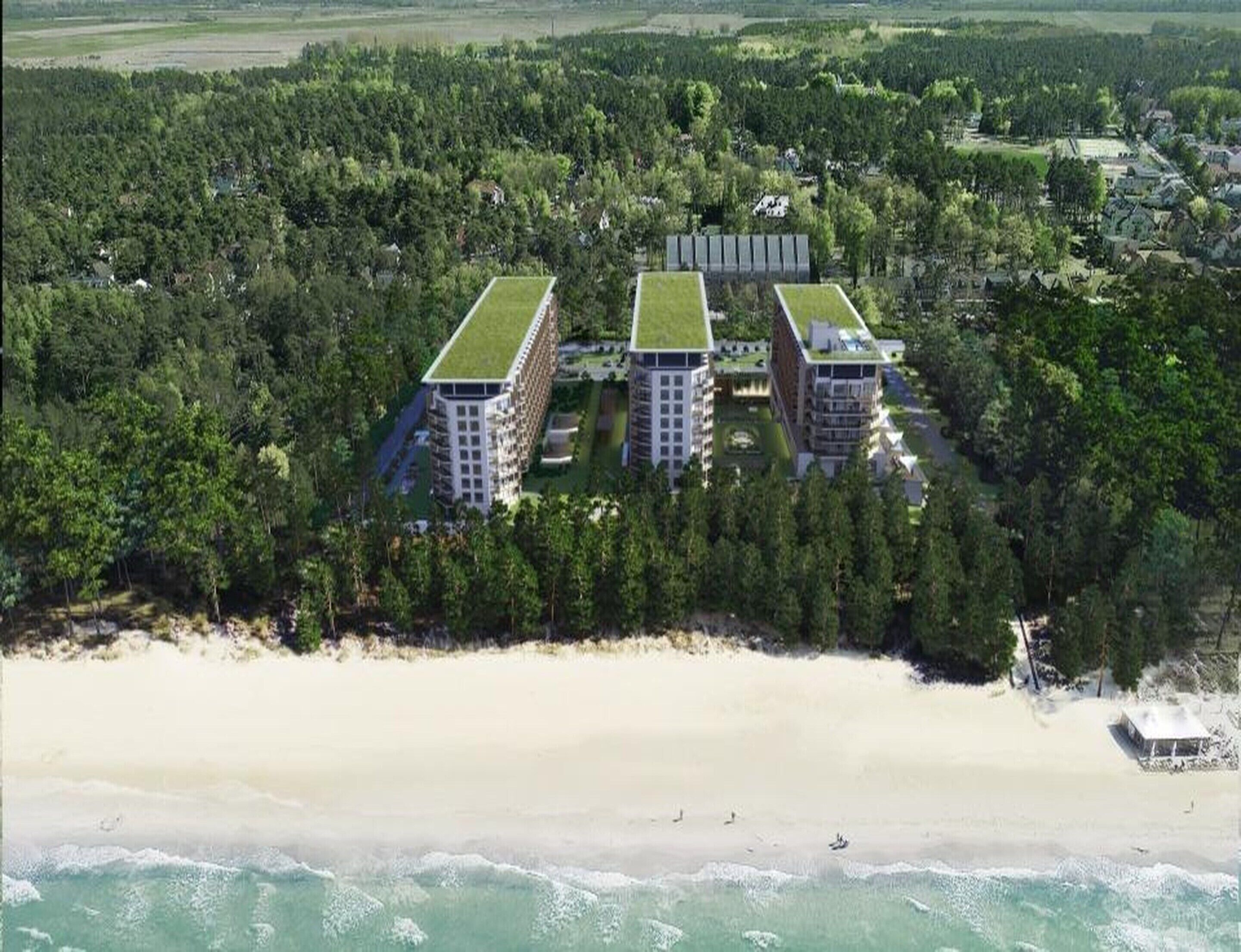 A coastal hotel with three buildings, each featuring a green roof, surrounded by dense forest and a sandy beach.