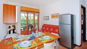 Ein Essbereich mit einem Holztisch, gedeckt für vier Personen, einem Kühlschrank und einem Fenster mit Vorhängen.