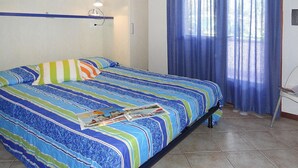 Ein Schlafzimmer mit Bett, Nachttisch, Fenster mit blauen Vorhängen und Wandregal mit Lampe.