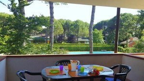Ein Balkon mit Tisch für Zwei, umgeben von Stühlen, mit Blick auf einen Swimmingpool und einen gepflegten Garten.