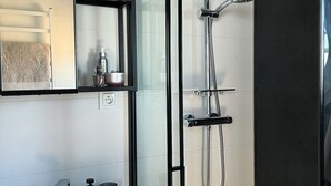 A modern bathroom with a glass shower enclosure, a towel rack, and a shelf with toiletries. - Houseboat in Lazy by Lake Jamno and Sea (gmina Sianów)