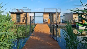 A wooden dock leading to a modern building with a view of a calm lake. - Houseboat in Lazy by Lake Jamno and Sea (gmina Sianów)