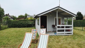 Ett litet hus med en veranda och två randiga trädgårdsstolar i förgrunden.