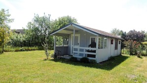 Ett litet hus i en våning med en veranda, omgivet av en gräsyta och träd.