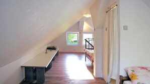 Un couloir étroit et incliné, doté d’un plancher en bois, d’un banc et d’un lit avec une literie à motifs floraux.