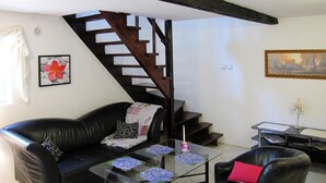 Un salon avec un canapé en cuir noir, une table basse en verre, un fauteuil en cuir noir, un escalier en bois et un tableau accroché au mur.