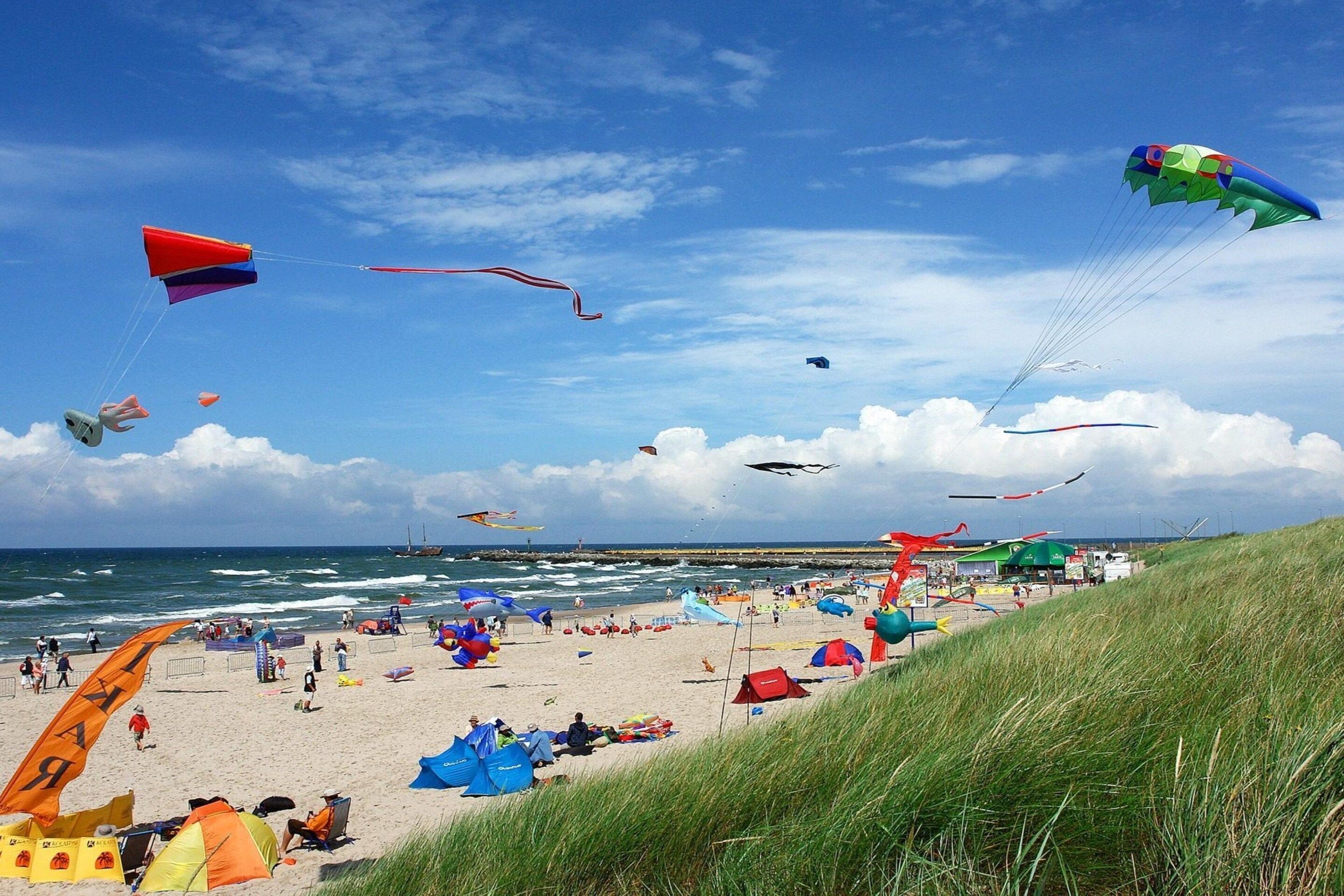 A beach with tents and people, and kites flying in the sky.