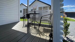A covered outdoor area with a wooden deck, two metal chairs, a small table, and a potted plant. - Holiday Homes Close to the Seaside Beach (Darlowo)