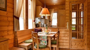 Interior acolhedor de uma cabana de madeira, com uma mesa de jantar posta para dois, um banco e uma área de cozinha com uma luminária pendente.