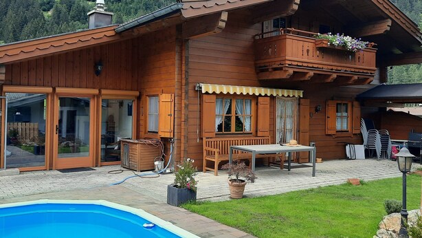 A wooden chalet with a swimming pool, a balcony with flowers, and a mountain backdrop. - Holiday Home, Krimml (Krimml)
