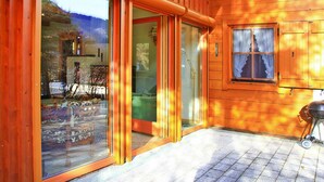 A wooden cabin with large sliding glass doors, a small window with curtains, and a barbecue grill outside. - Holiday Home, Krimml (Krimml)