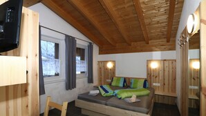 A wooden cabin room with a bed, a chair, a table, and a TV.