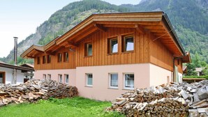 A wooden chalet with a sloped roof, multiple windows, and a view of a mountainous landscape.