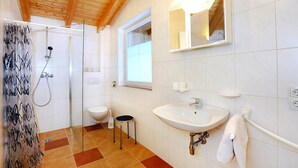 A bathroom with a shower, toilet, sink, and a small stool.