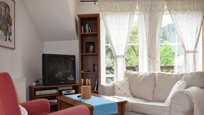 Un salon avec un téléviseur, une bibliothèque, un canapé blanc et un fauteuil rouge.
