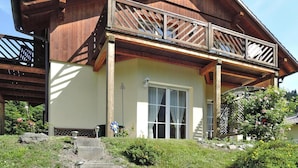 Un chalet en bois à deux étages, doté d’un balcon, d’une grande fenêtre et d’un chemin en pierre menant à l’entrée.