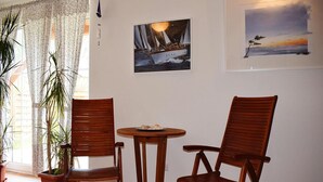 Une pièce comprenant deux chaises en bois et une petite table ronde, une plante en pot et deux œuvres d’art encadrées accrochées au mur.