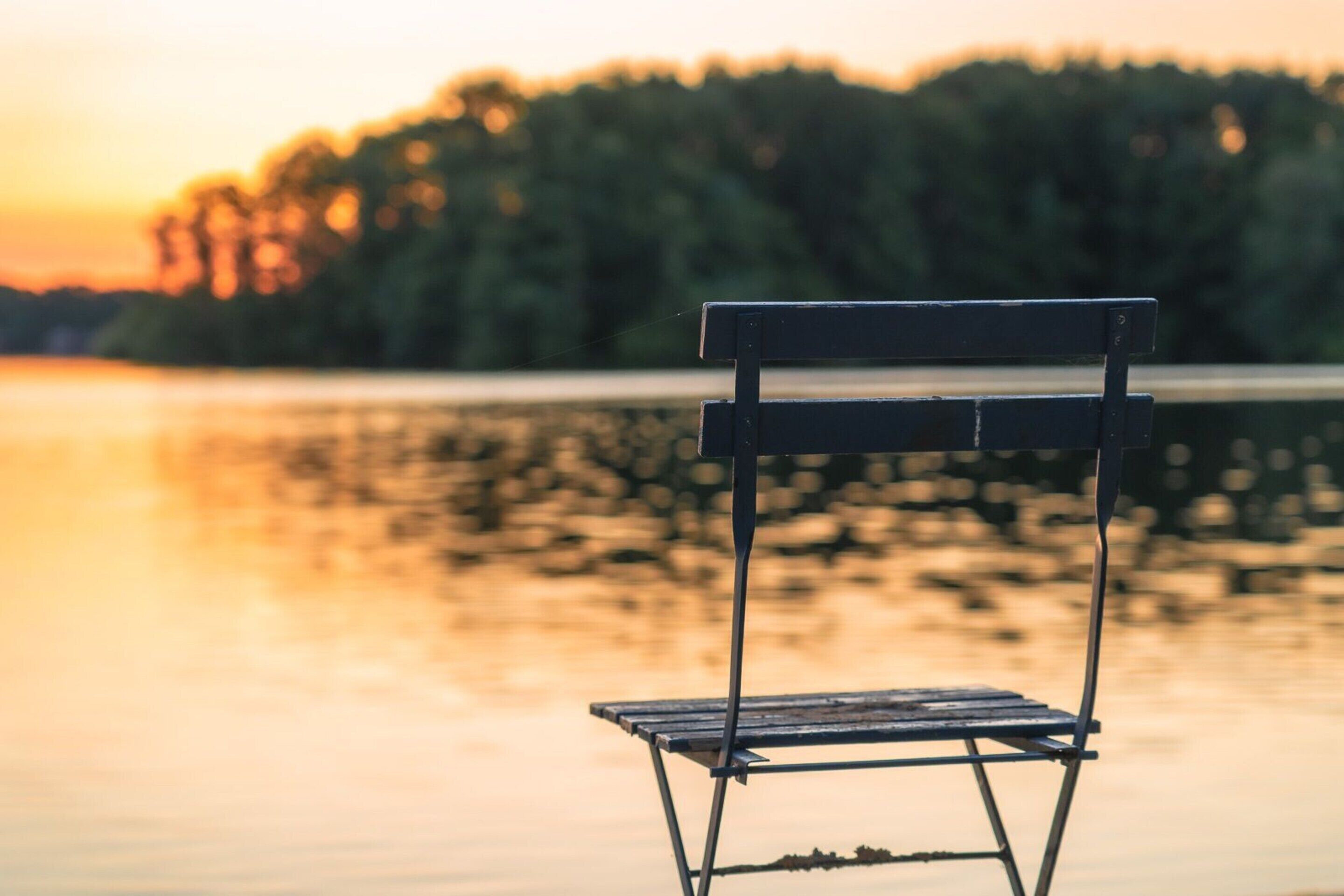 Ein metallischer Klappstuhl am See bei Sonnenuntergang.