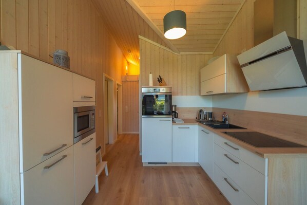 Une cuisine moderne avec des murs recouverts de panneaux en bois, un four encastré, un four à micro-ondes et un évier.