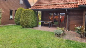 Ett trähus med ett tak täckt av takpannor, en inglasad veranda med en bänk och en välskött gräsmatta.