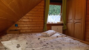 Ett mysigt sovrum på vinden med ett sluttande tak, en säng med mönstrat sänglinne, ett nattduksbord med en lampa och ett fönster med gardiner.