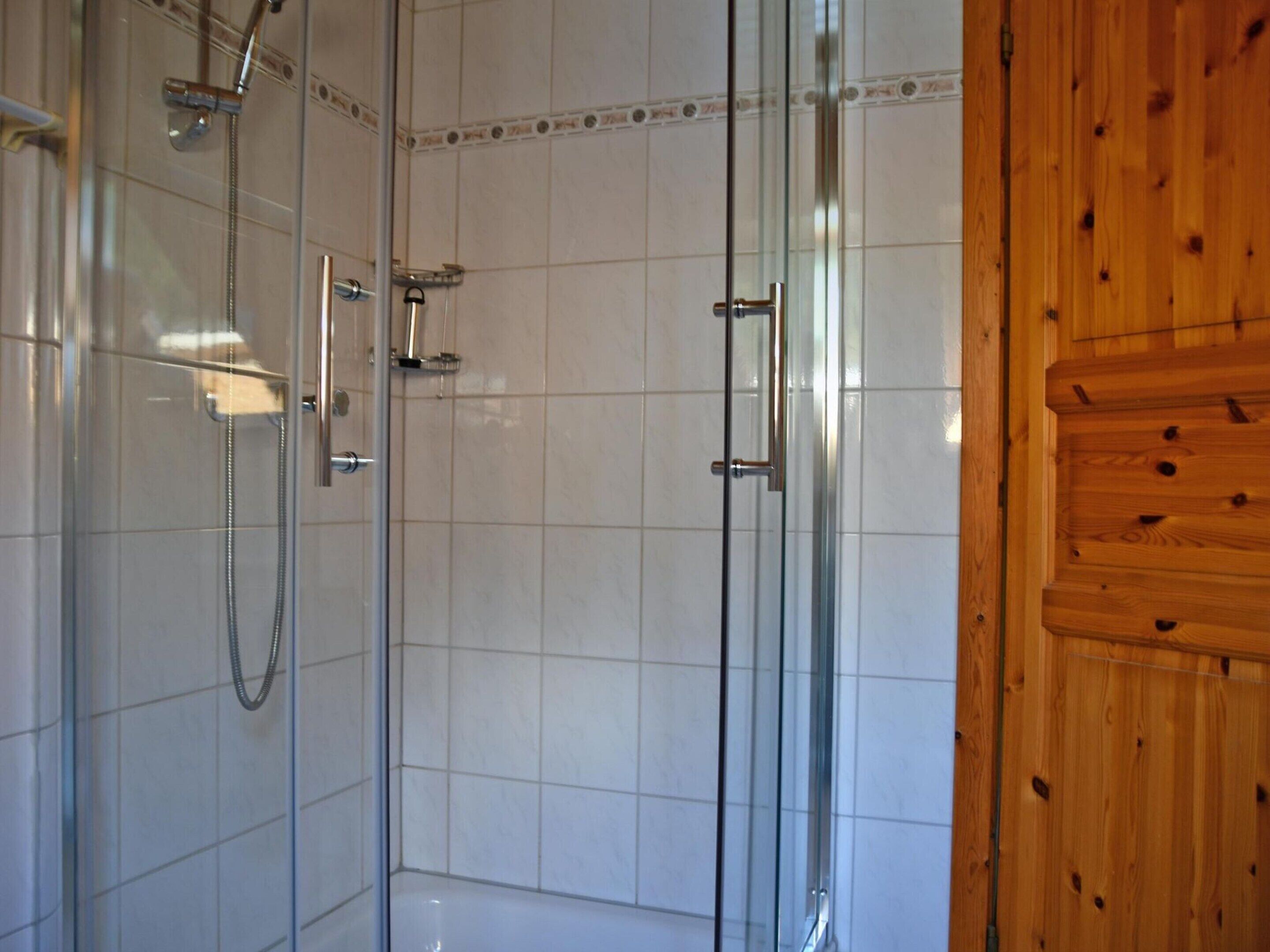 A glass-enclosed shower with a handheld showerhead and a wall-mounted faucet.