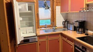 Ett kompakt kök med träskåp, en inbyggd ugn, en kaffebryggare och ett fönster med persienner.
