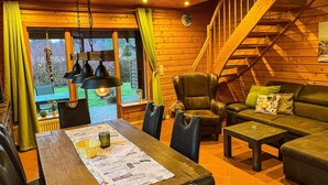 En mysig stuga med en inredning som inkluderar en trätrappa, en matplats med bord och stolar samt en sittgrupp med en soffa och fåtöljer.