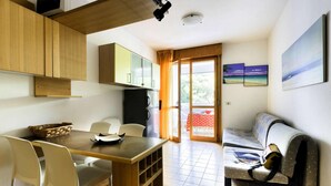 A compact living space with a dining area, a kitchenette, and a seating area with a view. - Condominio Quercia in Bibione Lido del Sole (San Michele al Tagliamento)