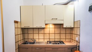 A compact kitchen with a gas stove, a sink, and wooden cabinets. - Condominio Quercia in Bibione Lido del Sole (San Michele al Tagliamento)