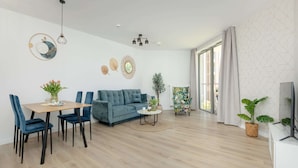 A modern living room with a blue sofa, dining table, chairs, and a TV. - Apartment in Pobierowo Near Baltic Beach (Rewal)
