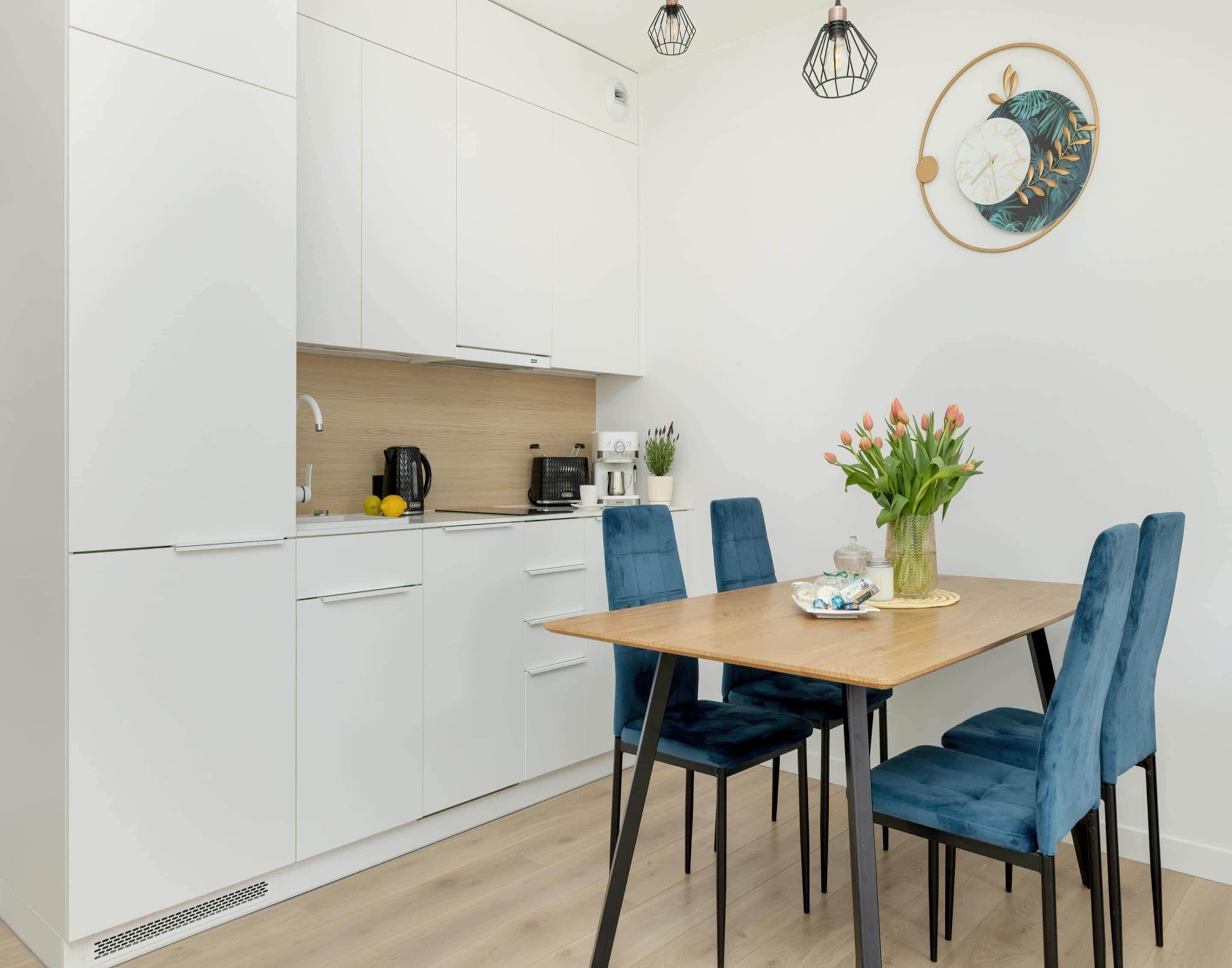 A modern kitchen with white cabinets, a wooden countertop, and a dining area with a wooden table and blue chairs.