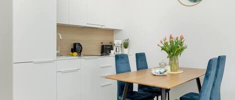 A modern kitchen with white cabinets, a wooden countertop, and a dining area with a wooden table and blue chairs.