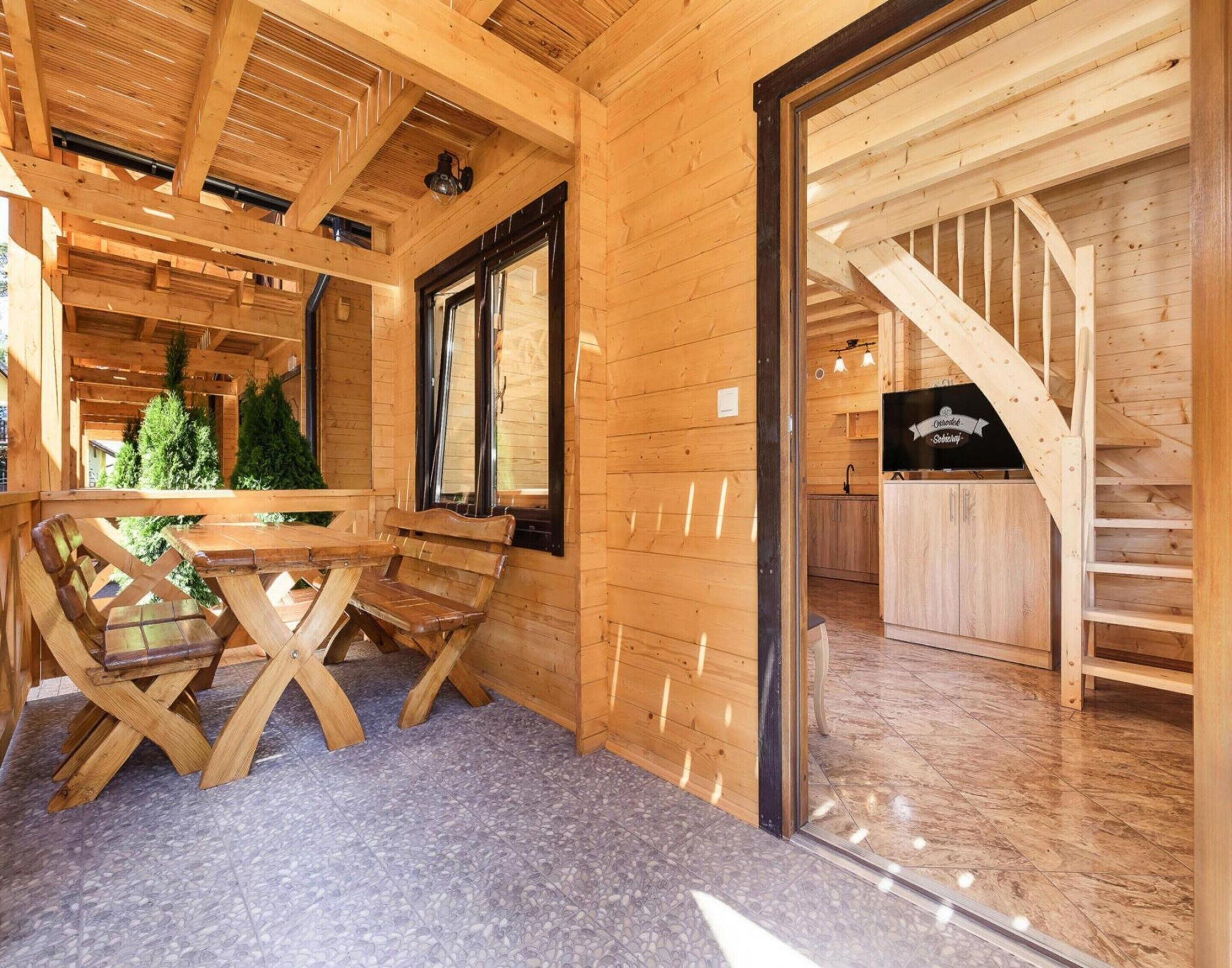 A wooden cabin interior with a dining area, a kitchen, and a staircase.
