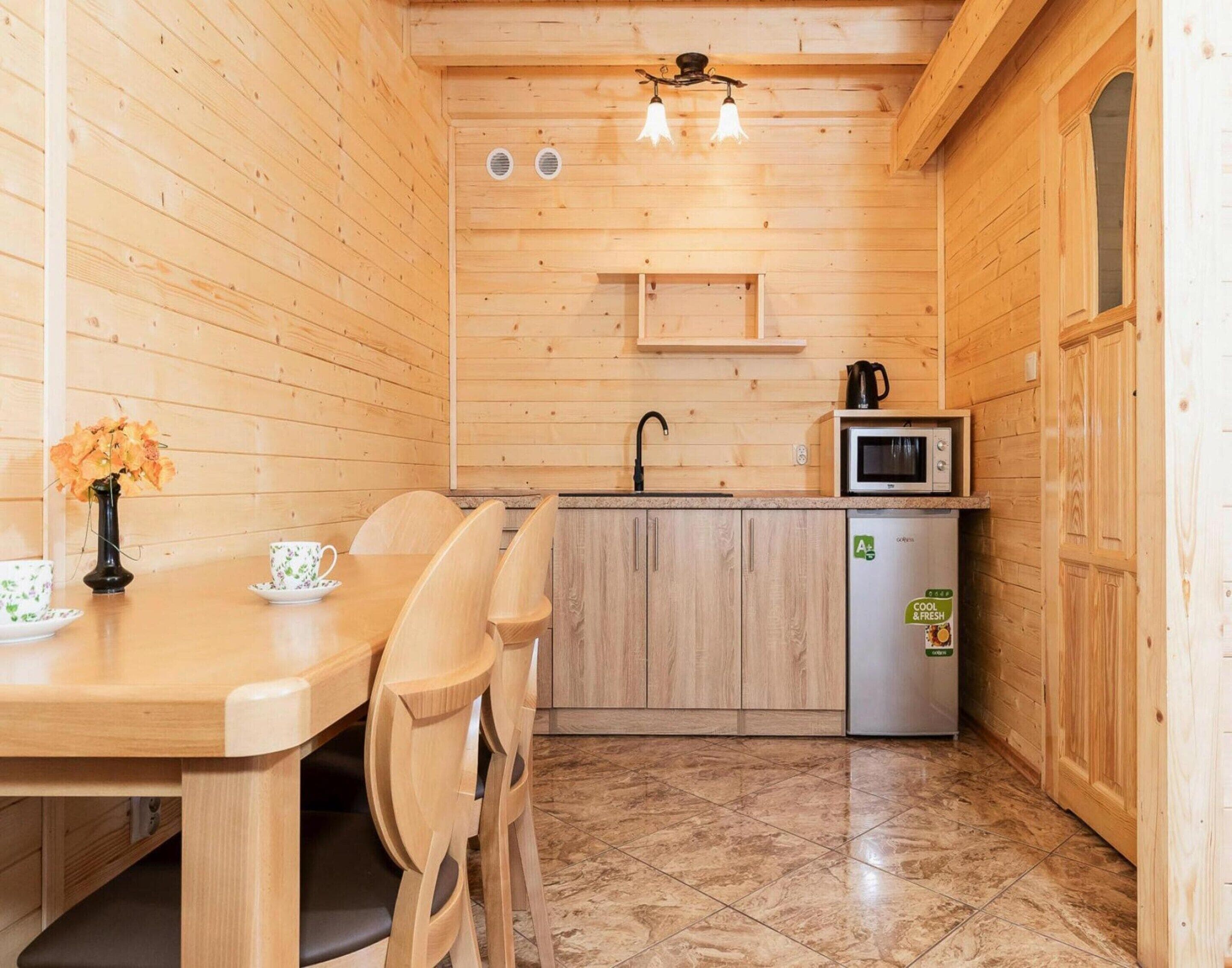 A wooden interior with a dining table, chairs, a kitchen area with a microwave, and a refrigerator.