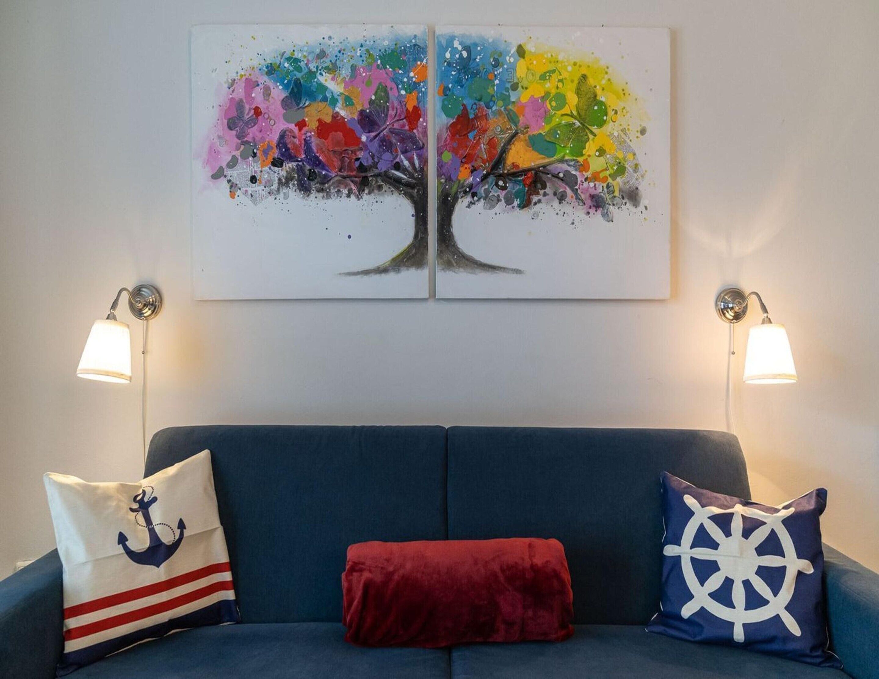 A room with a blue sofa, two wall-mounted lamps, and a colorful abstract painting above the sofa.