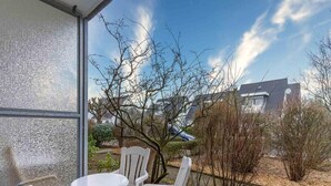Een terras met witte stoelen en een kleine tafel, met uitzicht op een tuin met bomen en een huis op de achtergrond.